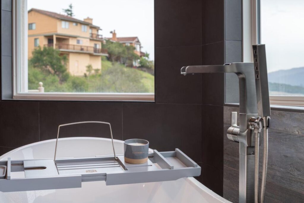 Professional bath remodel contractor created contemporary luxury with elegant freestanding tub, dramatic dark porcelain slabs, and striking matte black fixtures with scenic window views.