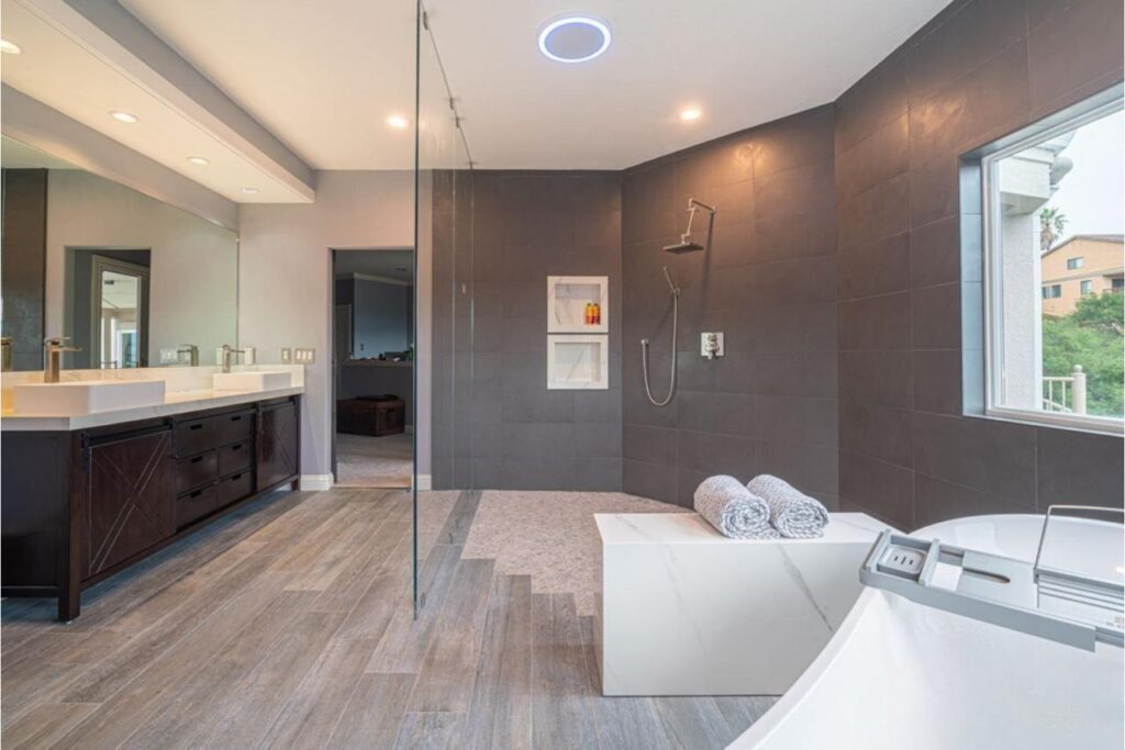 Expert bathroom remodel contractors delivered contemporary design with sculptural freestanding tub, dark porcelain slabs, warm wood flooring, and radiant heating system.