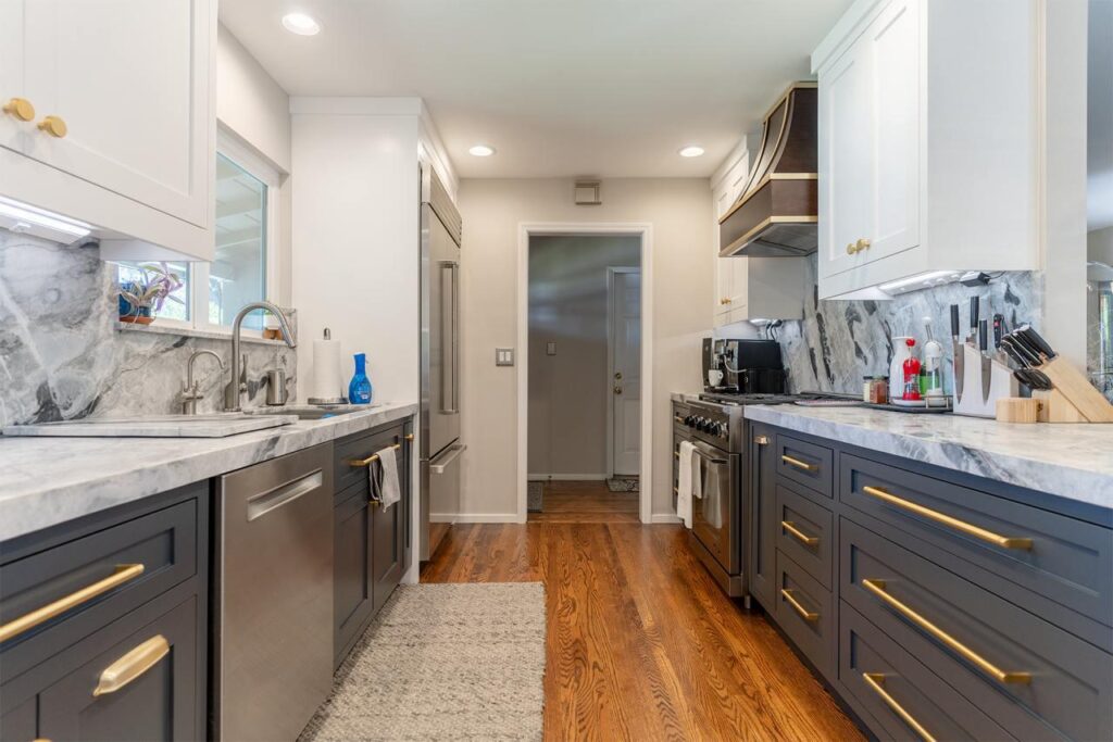 Sophisticated galley kitchen by kitchen remodeling contractors San Francisco showcasing navy cabinets with brass pendant lights and luxurious brass hardware throughout.