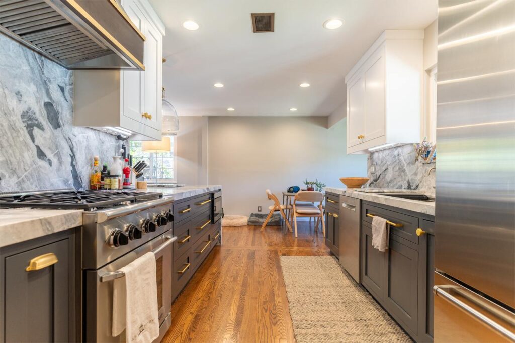 Kitchen remodeling in Santa Clara showcasing completed two-tone custom cabinetry with white shaker uppers and dark blue lowers, hardwood plank flooring, and professional-grade stainless steel appliances