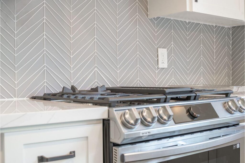 Shaker cabinets in San Francisco kitchen with gray finish, white herringbone tile backsplash, quartz countertops, and gas range by ASL Remodeling