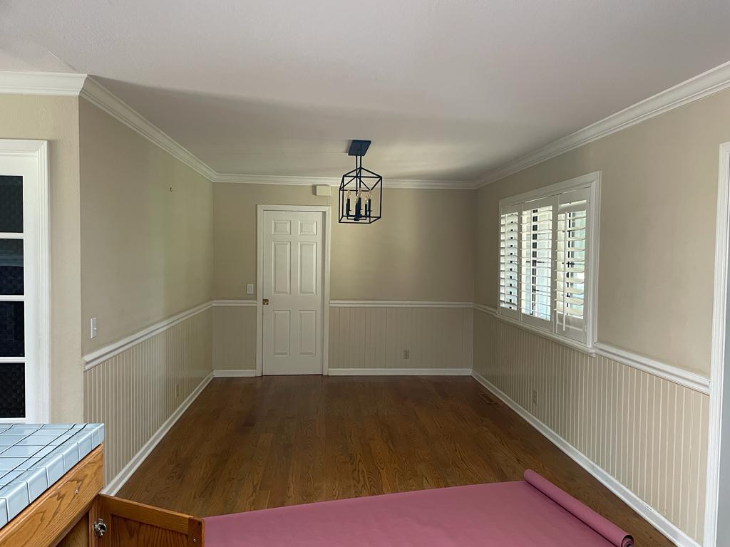 Before photo of Shulman Ave home remodel dining room showing original beige walls, white wainscoting, hardwood flooring, and plantation shutters prior to transformation