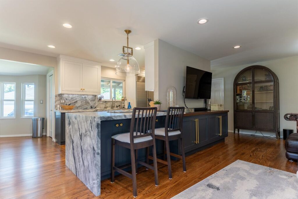 Transitional kitchen featuring navy blue island with marble countertops, pendant lighting, and open shelving with natural wood accents